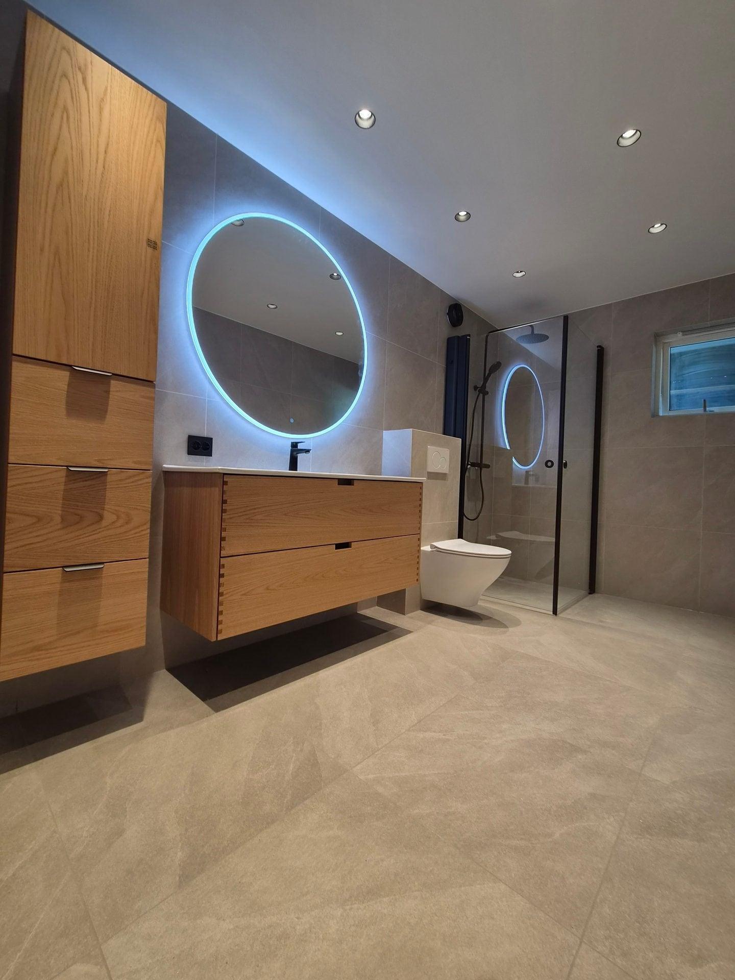 Ferdig bad med rundt, opplyst speil og innredning i tre
