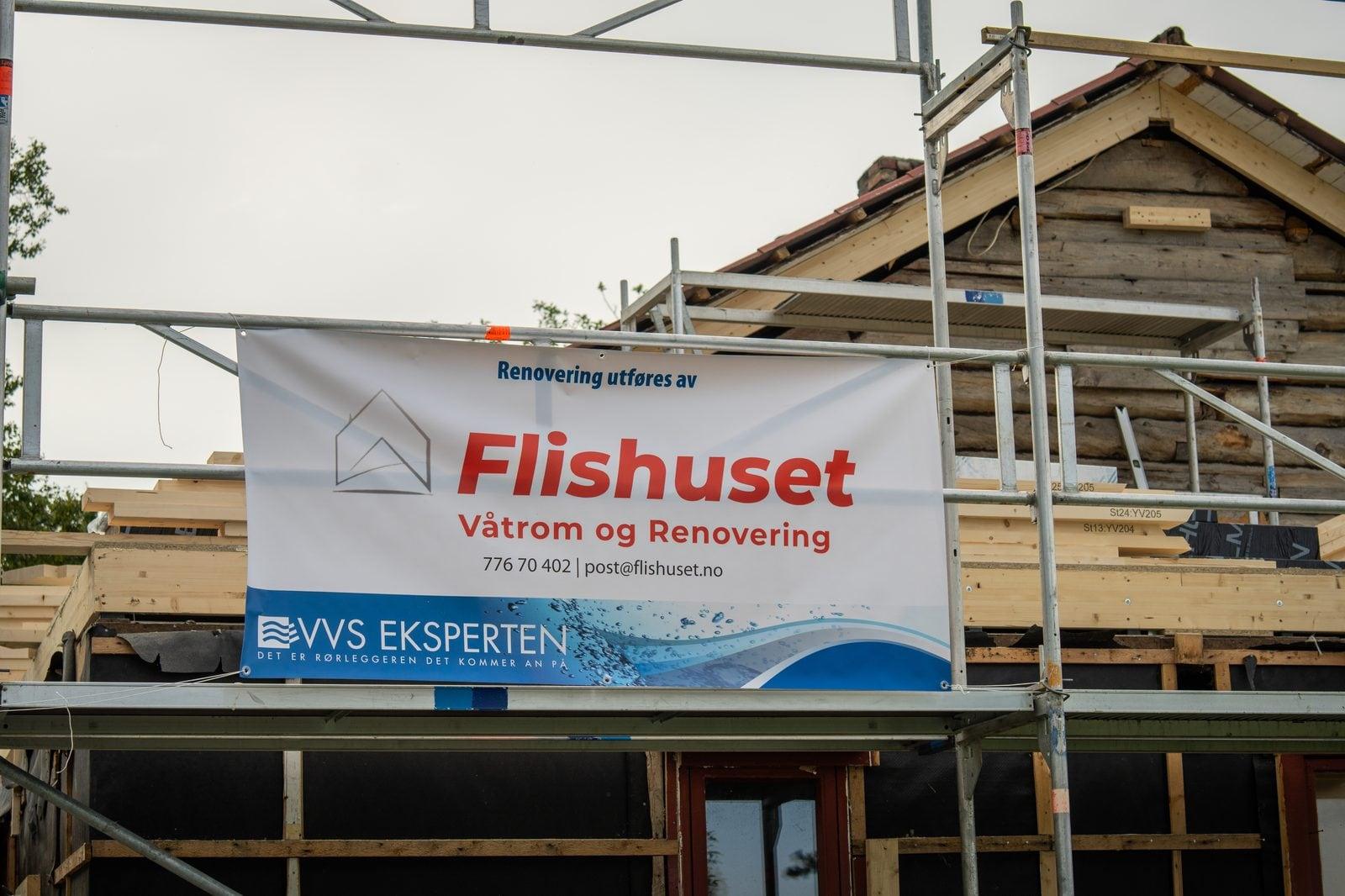 Flishuset-banner på stillaset rundt et tømmerhus under ombygging